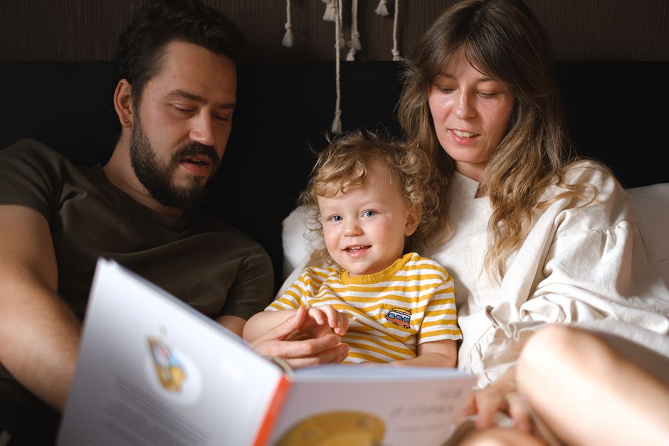 Langages de l’amour en famille : 5 repères et le piège des étiquettes A happy family reading together, featuring parents and their smiling child enjoying a book indoors.
