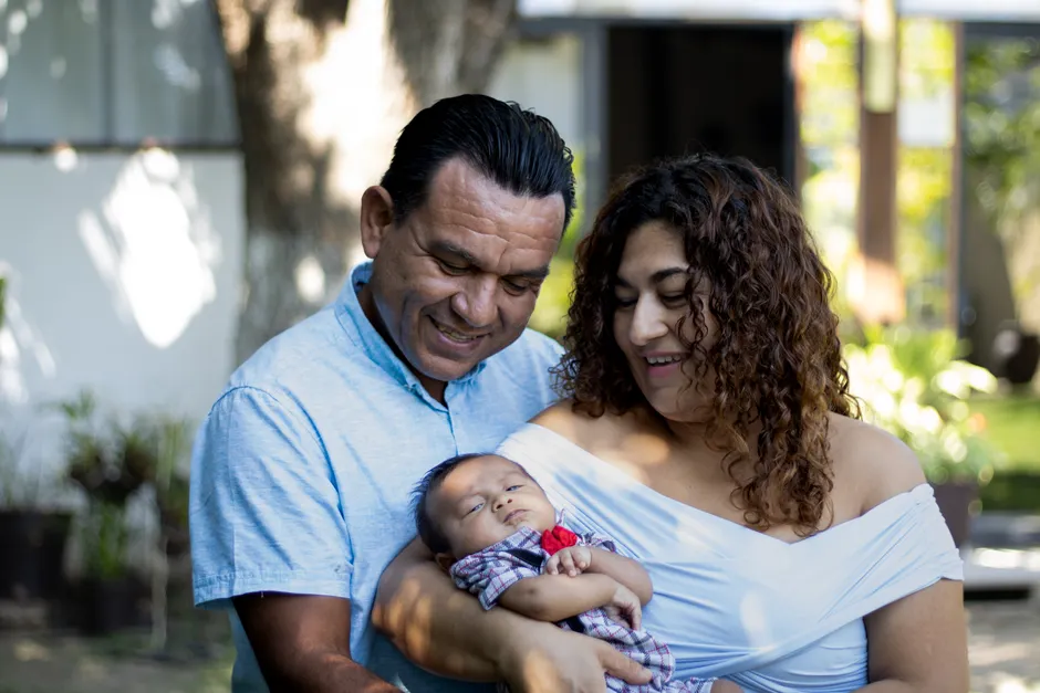 Après bébé, 7 signes d’une relation engagée, sans bague magique A joyful couple holding their sleeping baby in an outdoor setting, signifying love and family.