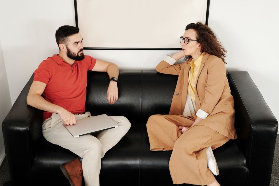 Compagnonnage ou relation : 5 repères pour y voir clair A man and woman sit on a black sofa, having a professional conversation.