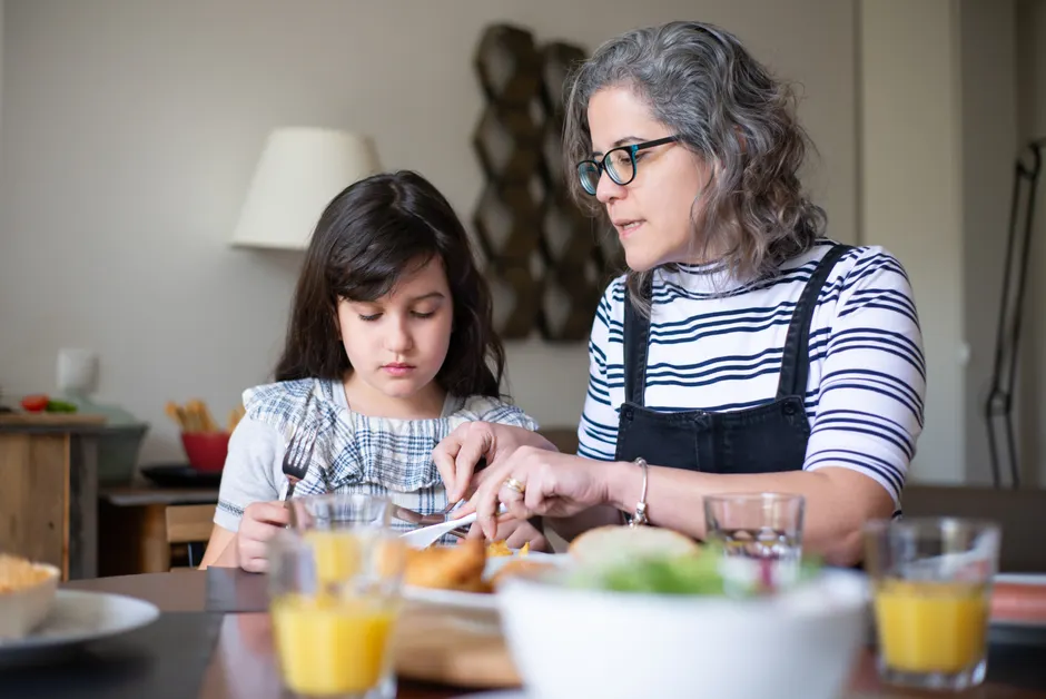 En Suède, chez les parents de 76 ans et plus, qui aide? Le lien n’est pas une dette A mother helps her daughter cut food during breakfast at home, fostering family bonding indoors.