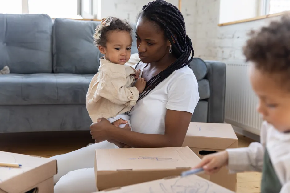 A mother holding her child with boxes around, depicting moving or family life at home.