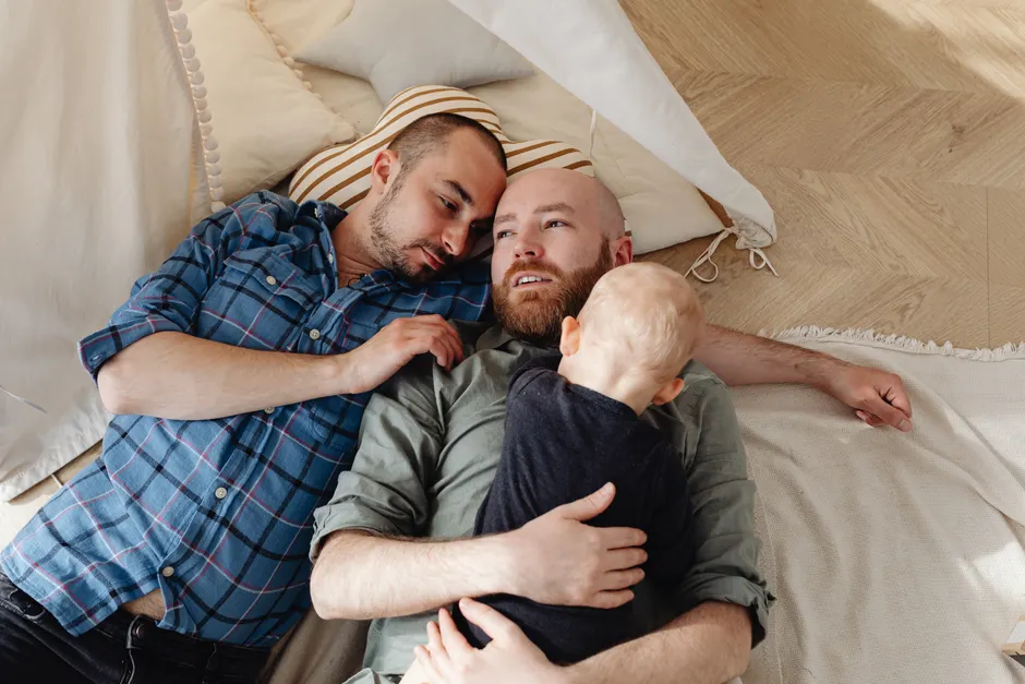 Après bébé, le couple change de tempo pendant 5 ans, et la vaisselle n’a pas tout le dossier A tender moment of a gay couple bonding with their child while resting indoors.