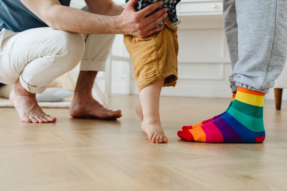 Dès 14 mois, bébé observe qui aide qui: le lien se construit sans mode d’emploi A toddler takes first steps with help from father indoors, showcasing love and support.