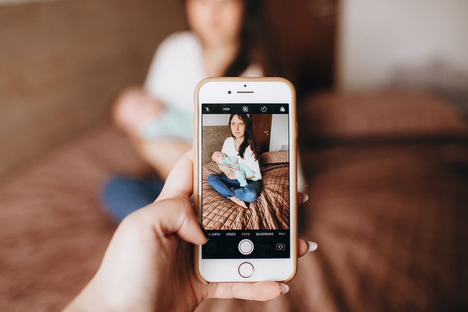 Réseaux sociaux et couple après bébé : 5 repères sans procès A woman sitting with her baby, captured through a smartphone camera indoors.