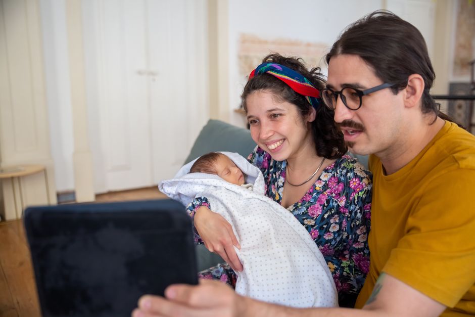 Après bébé, 6 gestes pour être un meilleur partenaire A young couple joyfully video chatting with their newborn baby in a cozy home setting.