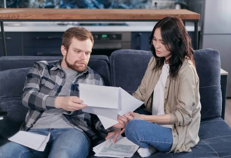 Couple et santé : 4 repères pour partager la charge mentale Asian woman and Caucasian man discussing taxes on couch.