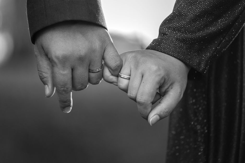 Bague de promesse : 5 repères avant de l’offrir Black and white image of couple holding hands, showcasing engagement rings, symbolizing commitment and love.