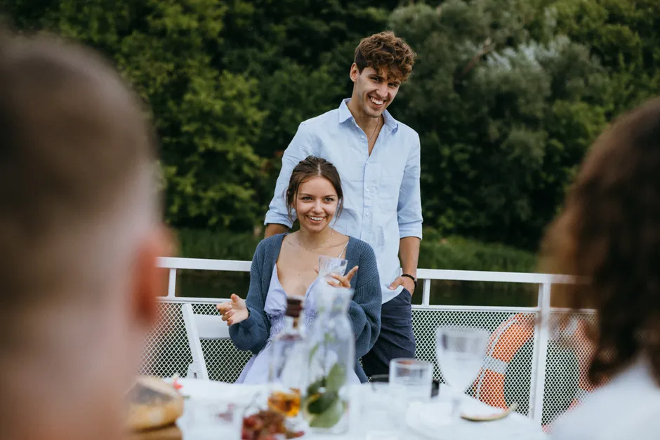 Lune de miel : 15 questions pour parler d’amour, de sexe et du quotidien sans interrogatoire Cheerful young couple at an outdoor dinner with friends, enjoying lively conversation and good company.