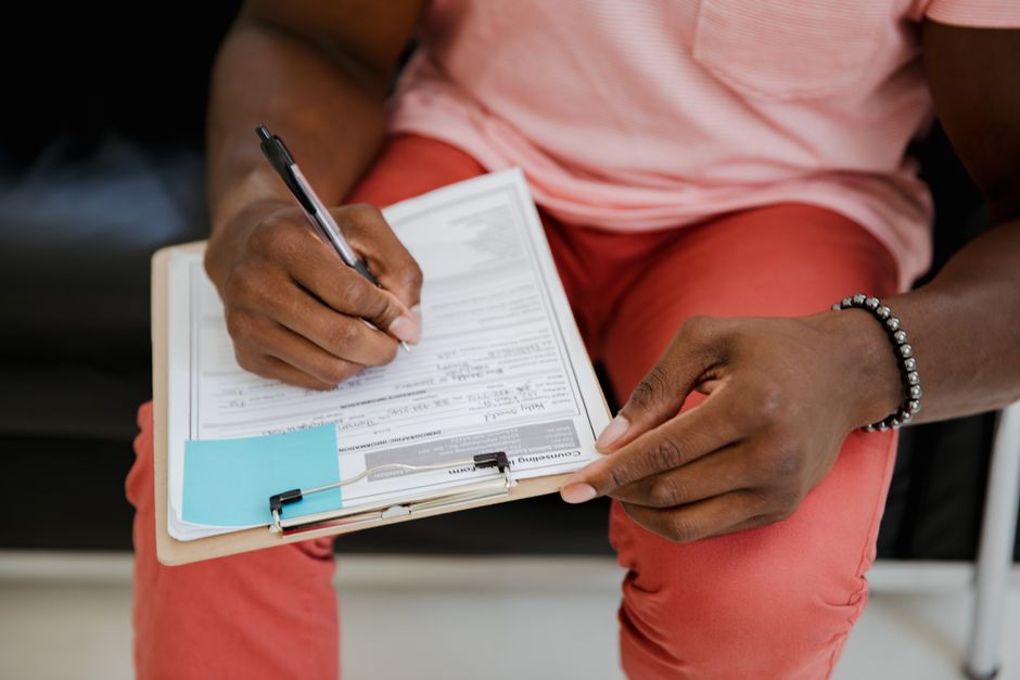 Close-up of a hand writing on a form with a pen attached to a clipboard.