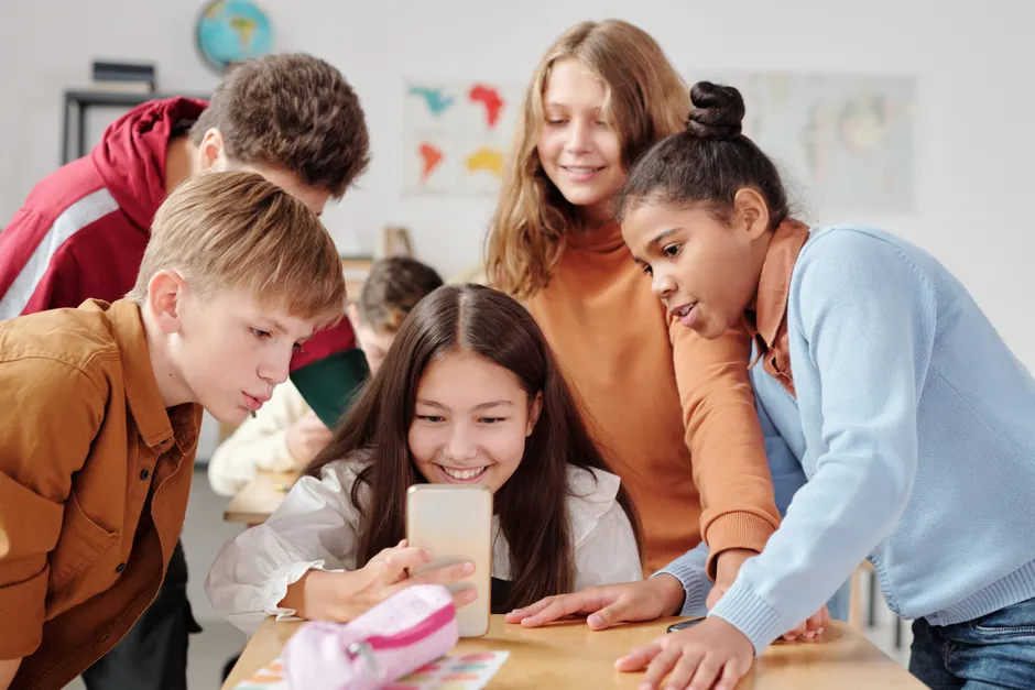 À 13-14 ans, SPARX n’a pas réduit les symptômes dépressifs en 12 mois Group of teenagers in a classroom setting happily gathered around a smartphone.
