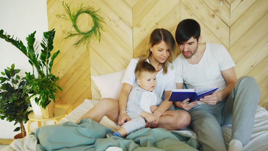 5 résolutions de couple avec enfants qui tiennent après janvier Loving parents reading a book with their child in a cozy bedroom setting, promoting family bonding.