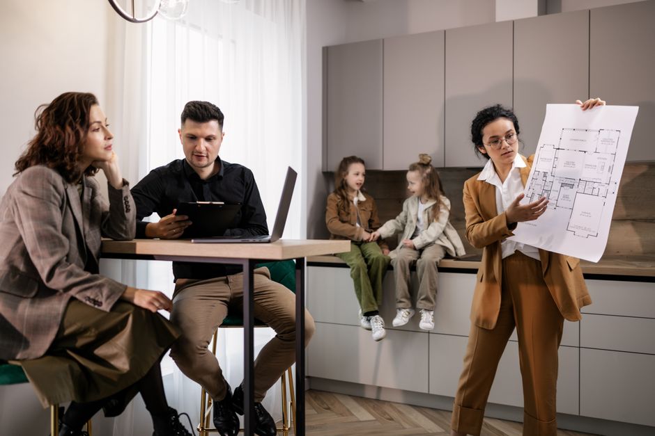 Couple durable : 5 repères quand tout déborde Real estate agent presenting house plans to clients in a modern kitchen setting.