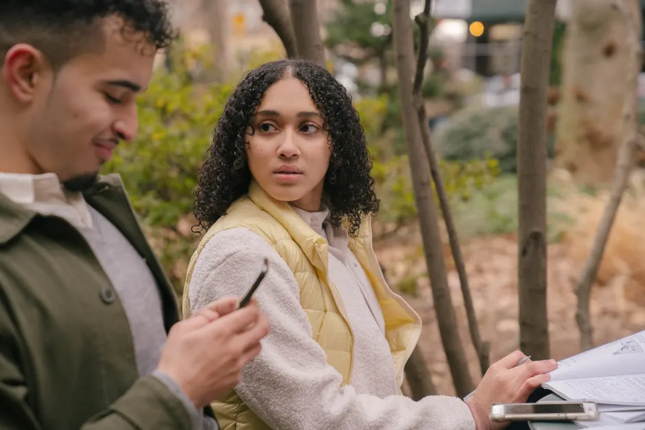 Communication de couple : 3 études, de la gratitude aux messages à distance Side view of Hispanic female sitting at table with textbooks while preparing for exams with phone while looking jealously at man texting on cellphone in daytime in park