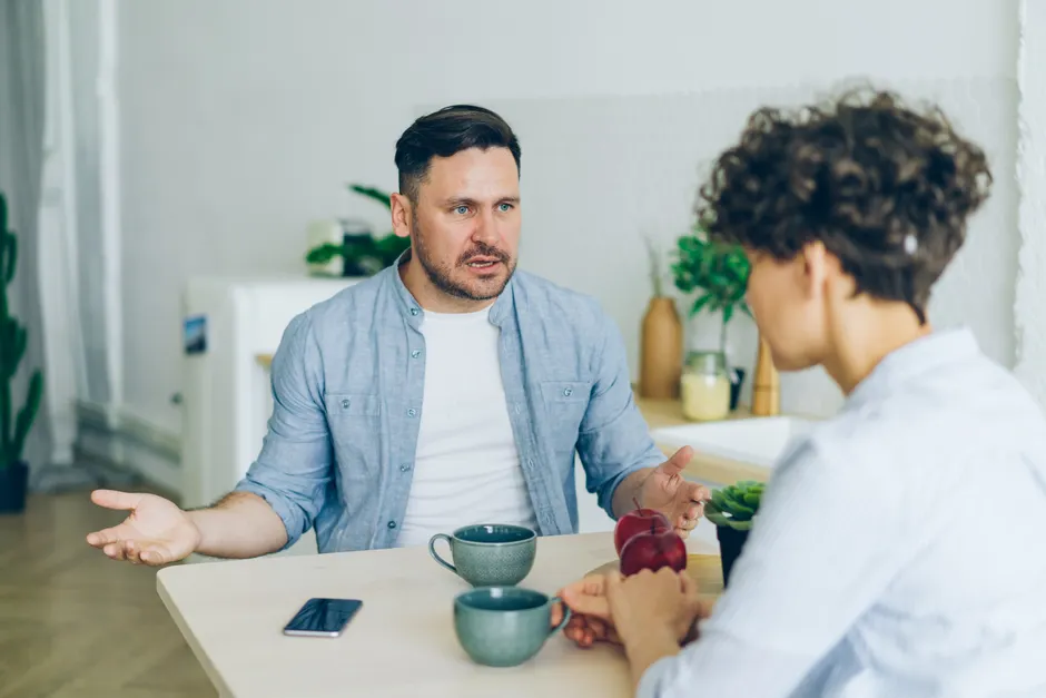Flamme jumelle : 15 questions pour parler sans se perdre Two adults engage in a conversation at a kitchen table with coffee cups.