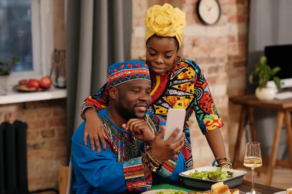 Relation à distance : 6 repères pour aimer sans GPS A joyful couple in colorful dashiki attire making a video call at a festive indoor gathering.