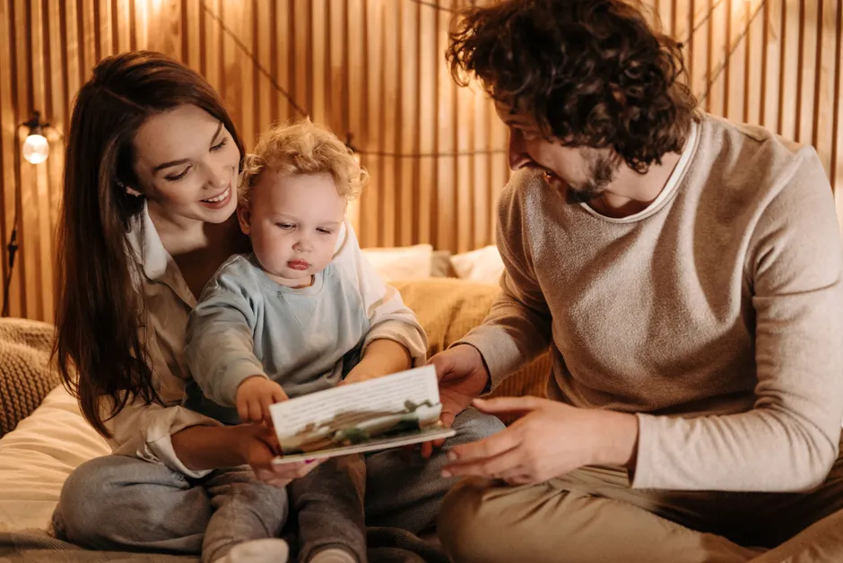 Après bébé : 5 repères pour l’égalité dans le couple, sans compter les bavoirs A joyful family bonding moment with parents and child reading in a cozy indoor setting.