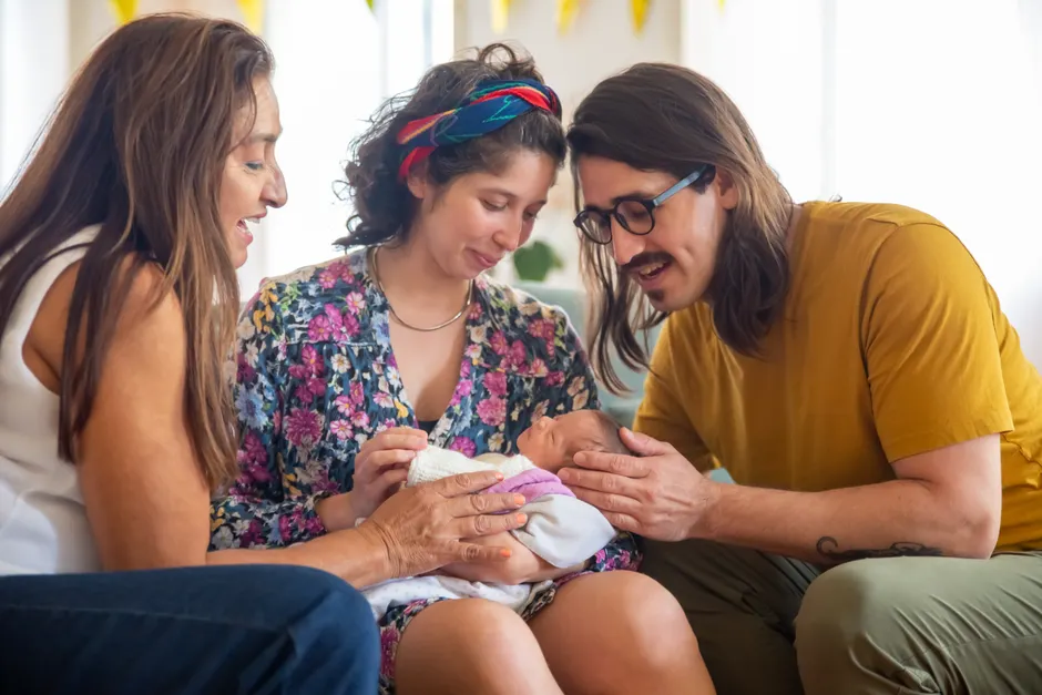A loving family of four adores their newborn in a cozy living room setting, capturing moments of joy and connection.