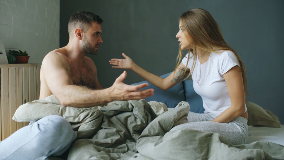 Communication dans le couple : 4 études, et le silence ne dit pas tout A young couple having a heated argument while sitting on a bed indoors.