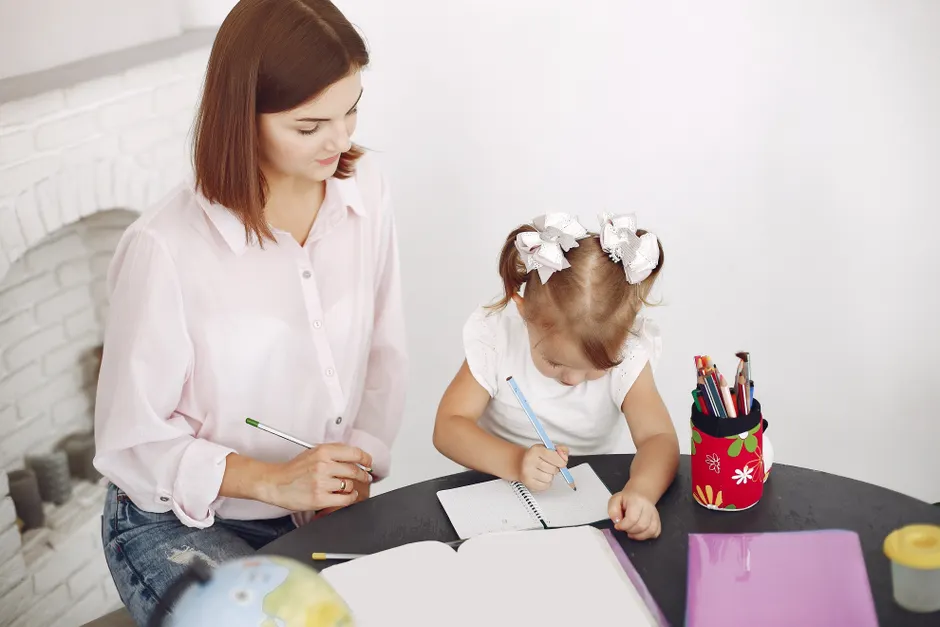 Écriture expressive : 15 minutes pour poser ses émotions, pas pour tout régler From above small girl drawing with pencil in notepad while mother sitting near at round table
